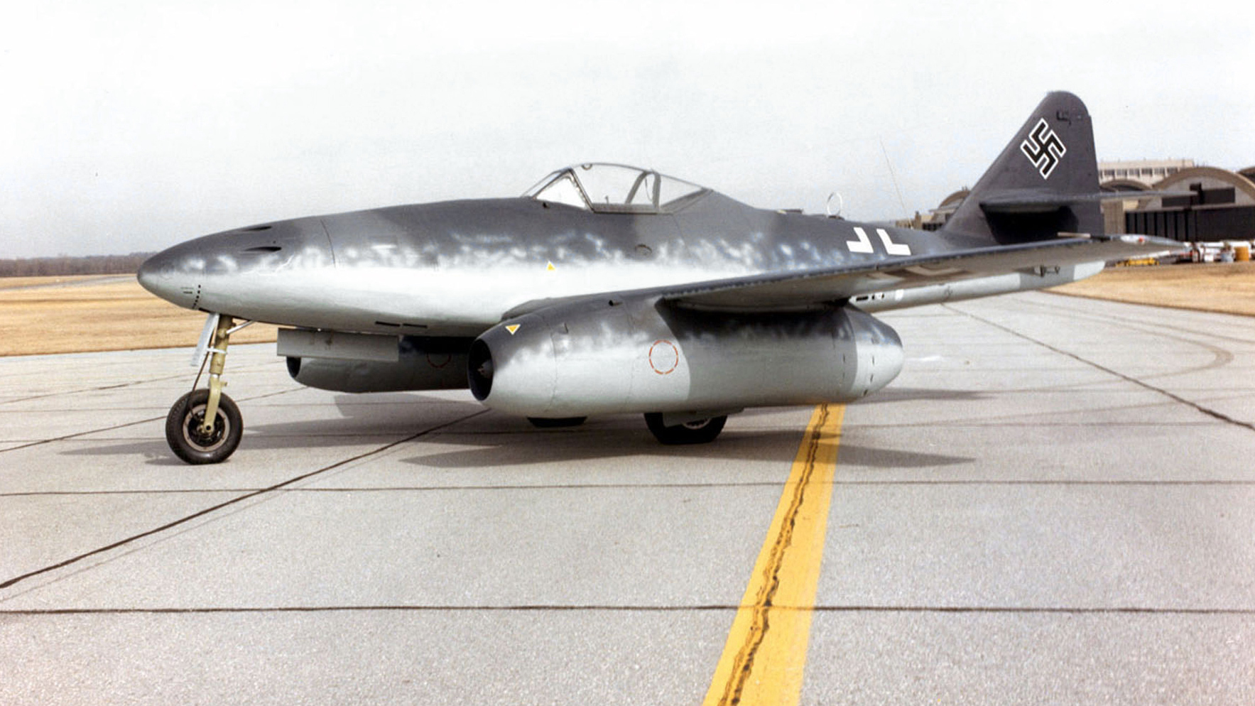 Insert image here: Woodland dispersal hardstand with Me 262; mechanics under camouflage netting, fuel bowser nearby.